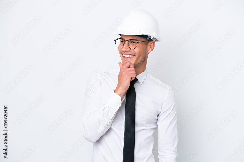 Young architect caucasian man with helmet and holding blueprints isolated on white background looking to the side and smiling