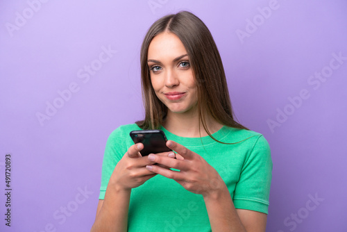 Young caucasian woman isolated on purple background sending a message with the mobile