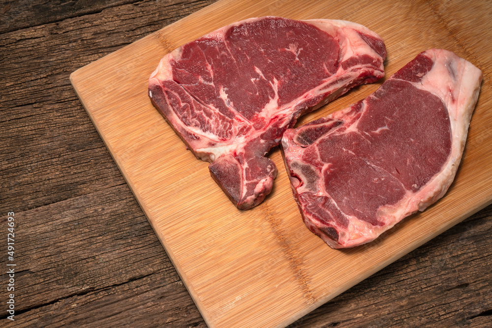 Raw fresh beef T-bone steak on wooden background, Close-up view of marble t-bone steak isolated on wooden background.