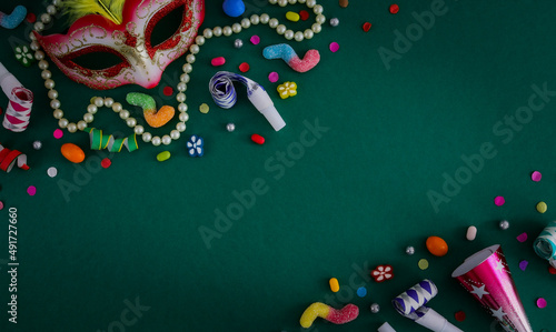 Masquerade mask  whistle  paper confetti  pipes  beads  feathers and candies on a dark green .
