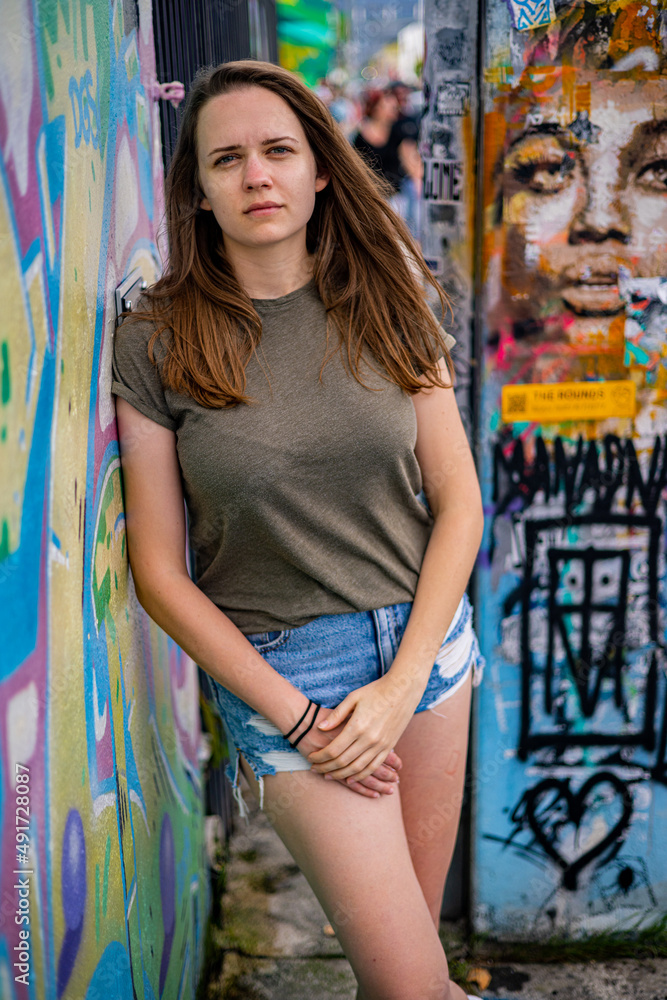 Naklejka premium Young and beautiful woman leans against a colorful wall and poses for the camera - typical street style - travel photography