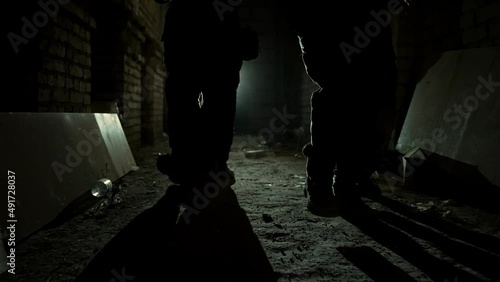 Group of armed men in camouflage carefully approach in corridor in light. A military group of men carefully walk towards the target at night in an abandoned facility High quality 4k footage