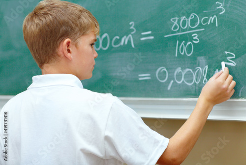 Hes a junior genius. Young schoolboy doing an equation on the blackboard at school. photo