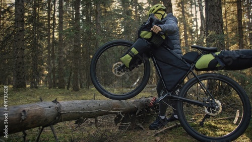 The woman travel on mixed terrain cycle touring with bike bikepacking outdoor. The traveler journey with bicycle bags. Stylish bikepacking, bike, sportswear in green black colors. Magic forest park. © ivandanru
