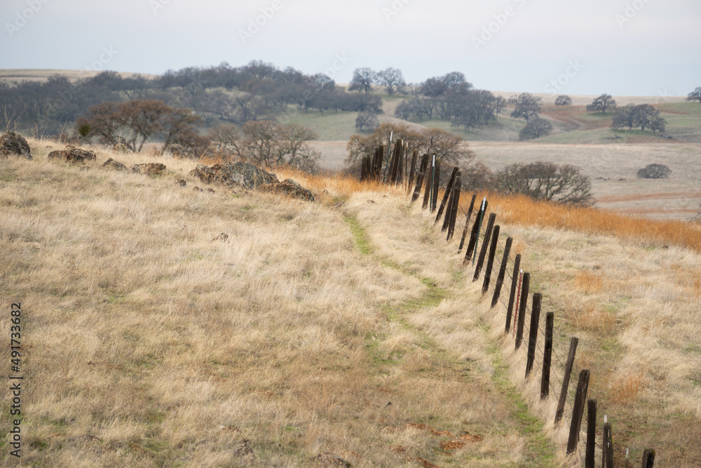 old wood post fence over rolling hills of  a dry grass pasture