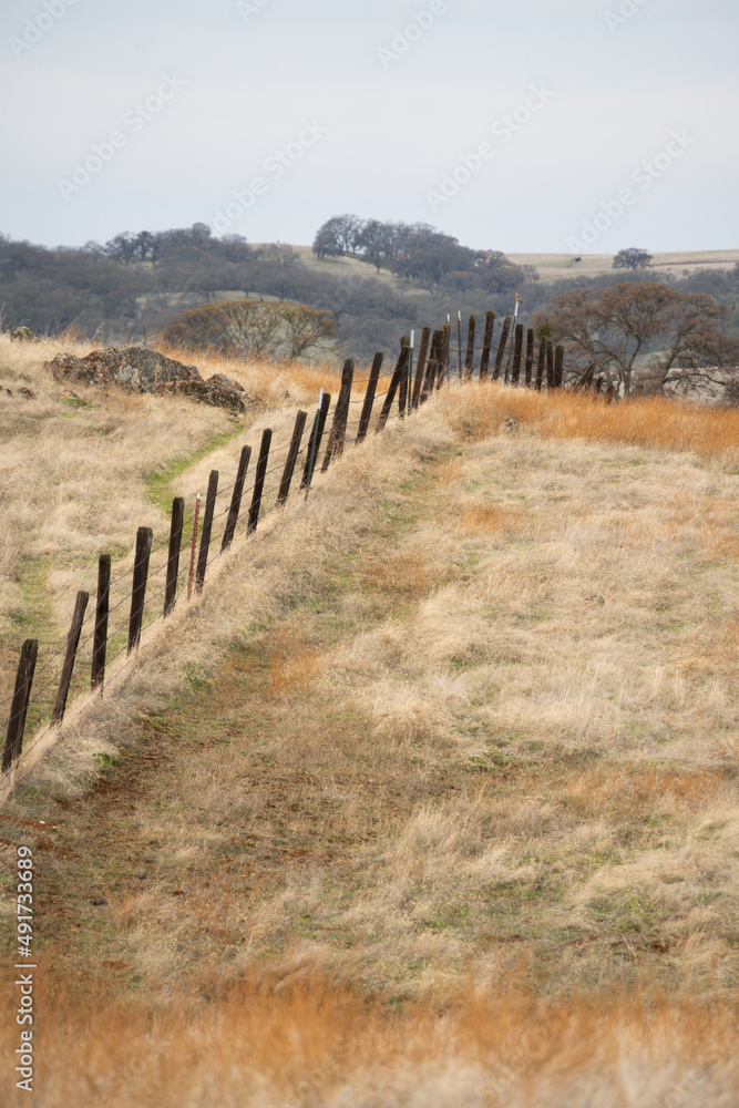 old wood post fence over rolling hills of  a dry grass pasture