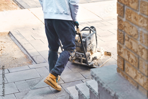 Landscaping worker contractor using plate compactor to apply polymeric joint sands on interlock pavers. Home garden and landscape renovation project background.  photo