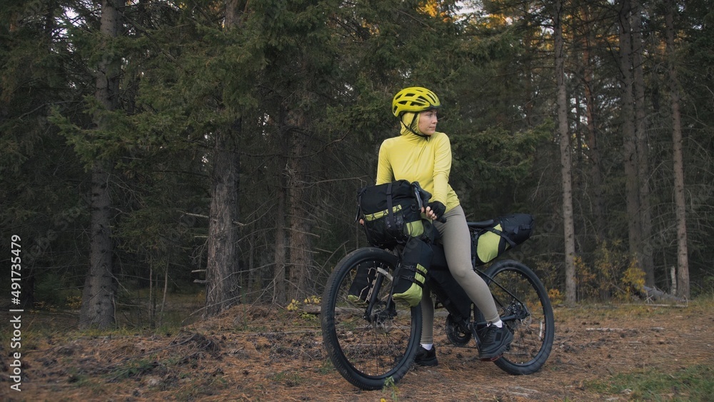 Fototapeta premium The woman travel on mixed terrain cycle touring with bike bikepacking outdoor. The traveler journey with bicycle bags. Stylish bikepacking, bike, sportswear in green black colors. Magic forest park.