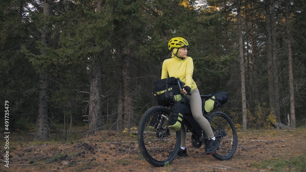 The woman travel on mixed terrain cycle touring with bike bikepacking outdoor. The traveler journey with bicycle bags. Stylish bikepacking, bike, sportswear in green black colors. Magic forest park.