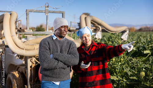 Fotografie Couple of skilled workers, man and woman, communicate near tractor with fumigato