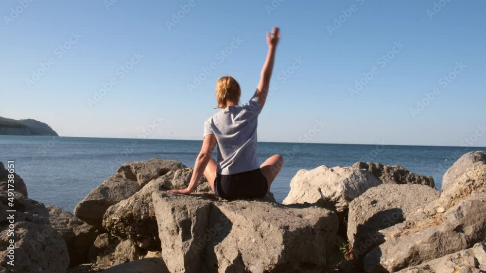 Young caucasian woman doing stretching exercises at the seashore. Girl meditating at the view of the ocean or sea at sunrise. Concept of yoga and solo activity. Meditation and healthy lifestyle. Young caucasian woman doing stretching exercises at the seashore. Girl meditating at the view of the ocean or sea at sunrise. Concept of yoga and solo activity. Meditation and healthy lifestyle.