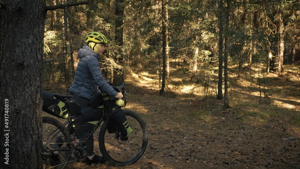 The woman travel on mixed terrain cycle touring with bike bikepacking outdoor. The traveler journey with bicycle bags. Stylish bikepacking, bike, sportswear in green black colors. Magic forest park.