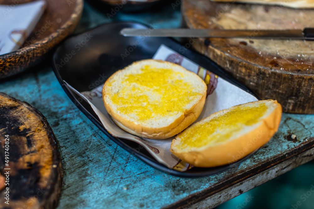 Closeup shot of delicious fresh baked tasty bread and burger bun with sesame topping in old wooden plate placed on round shape wood cutting board on dirty local restaurant counter Closeup shot of delicious fresh baked tasty bread and burger bun with sesame topping in old wooden plate placed on round shape wood cutting board on dirty local restaurant counter