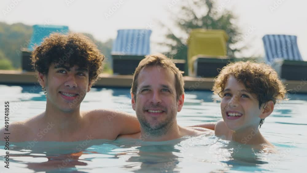 Portrait of father with two sons having fun in outdoor swimming pool on summer vacation together - shot in slow motion Portrait of father with two sons having fun in outdoor swimming pool on summer vacation together - shot in slow motion