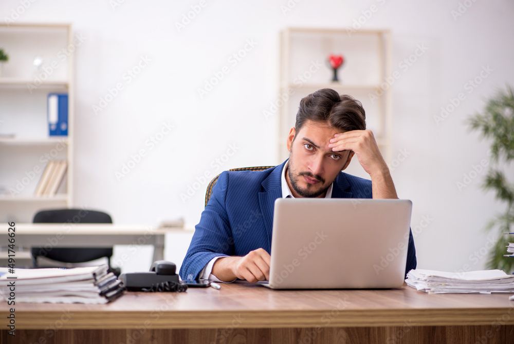 Young male employee unhappy with excessive work in the office Young male employee unhappy with excessive work in the office