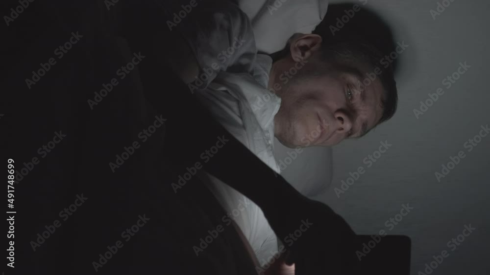 Vertical Video. Man Lying in Bed and Using Smartphone at Night, News and Social Media Addiction. Insomnia and Sleep Disorder Concept