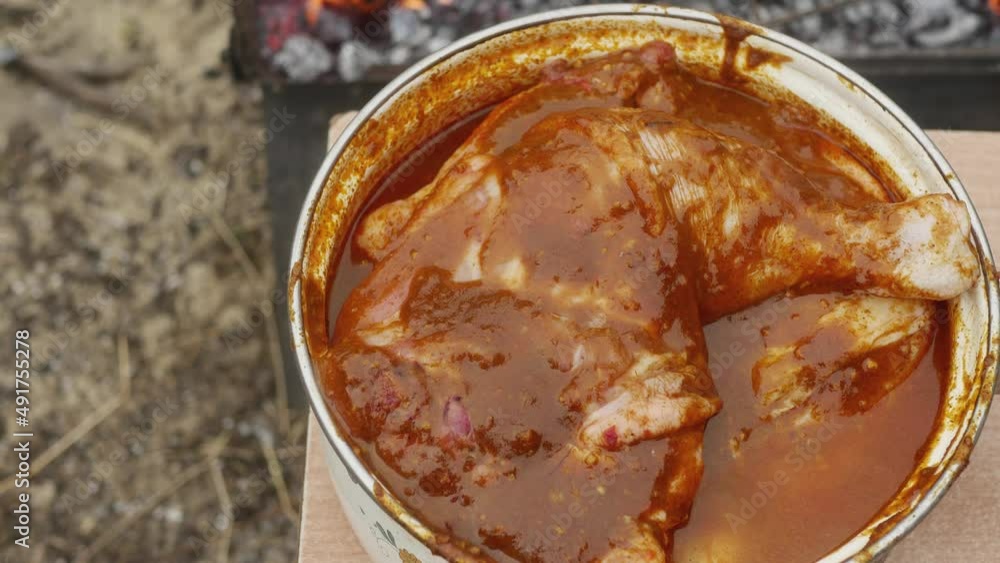 pot with marinated chicken legs on a bench near a hot portable barbecue pot with marinated chicken legs on a bench near a hot portable barbecue