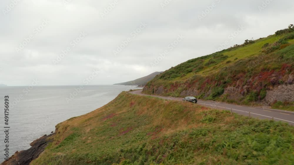 Forwards tracking of car on coastal road on cloudy day. Rocky sea coast with cliffs and grassy slope. Ireland Forwards tracking of car on coastal road on cloudy day. Rocky sea coast with cliffs and grassy slope. Ireland