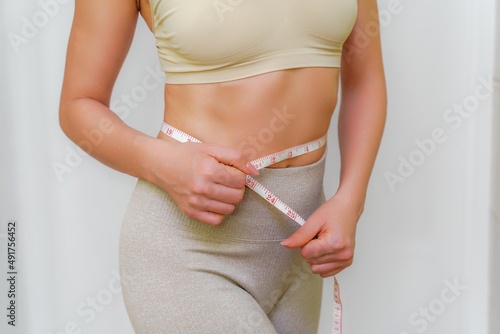 Close up of slim woman measuring her waist's size with tape measure. Isolated on white background.