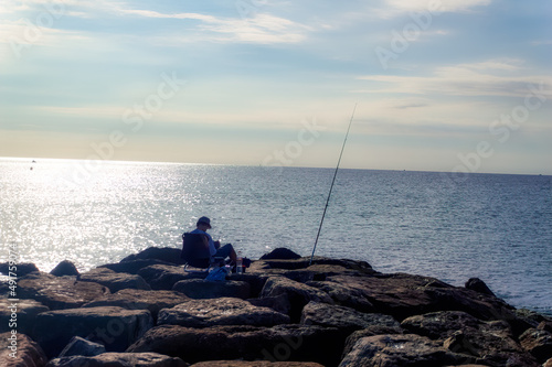People are fishing at rocky pier during summer morning in Cambrils, Spain.