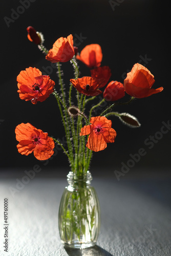 Glass bottle of red poppies stands on a black stone surface.