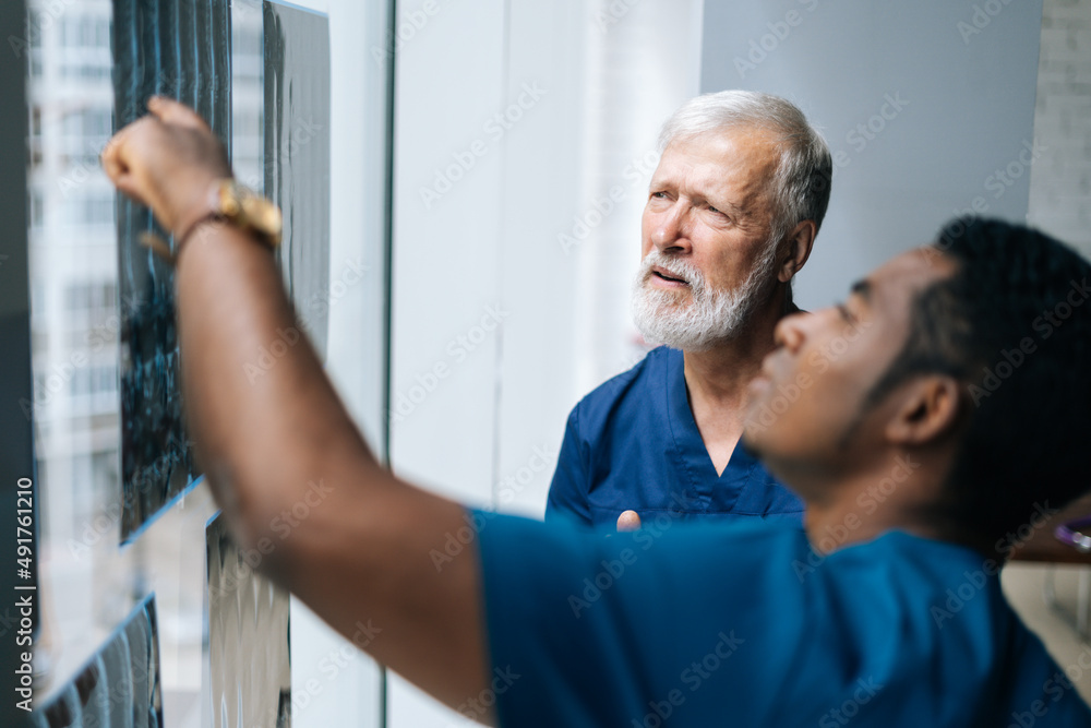 Obraz premium Close-up of team multiethnic doctors discussing together history disease of patient using MRI scan during medical meeting standing near window. Concept of medicine and health care.