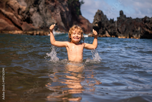 Happy kid have fun on tropical sea beach resort. Funny boy with splashes by water. Active kids lifestyle, swimming activity on summer holiday with children.