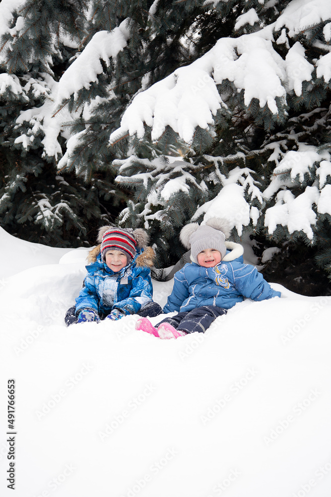 Children play in the snow against the background of snow-covered fir trees