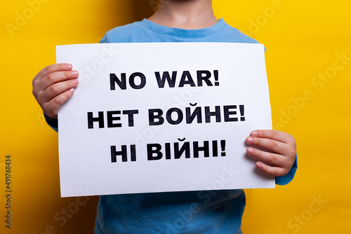 A child in a blue T shirt holds a poster with appeals for peace on a yellow background. no face, close-up