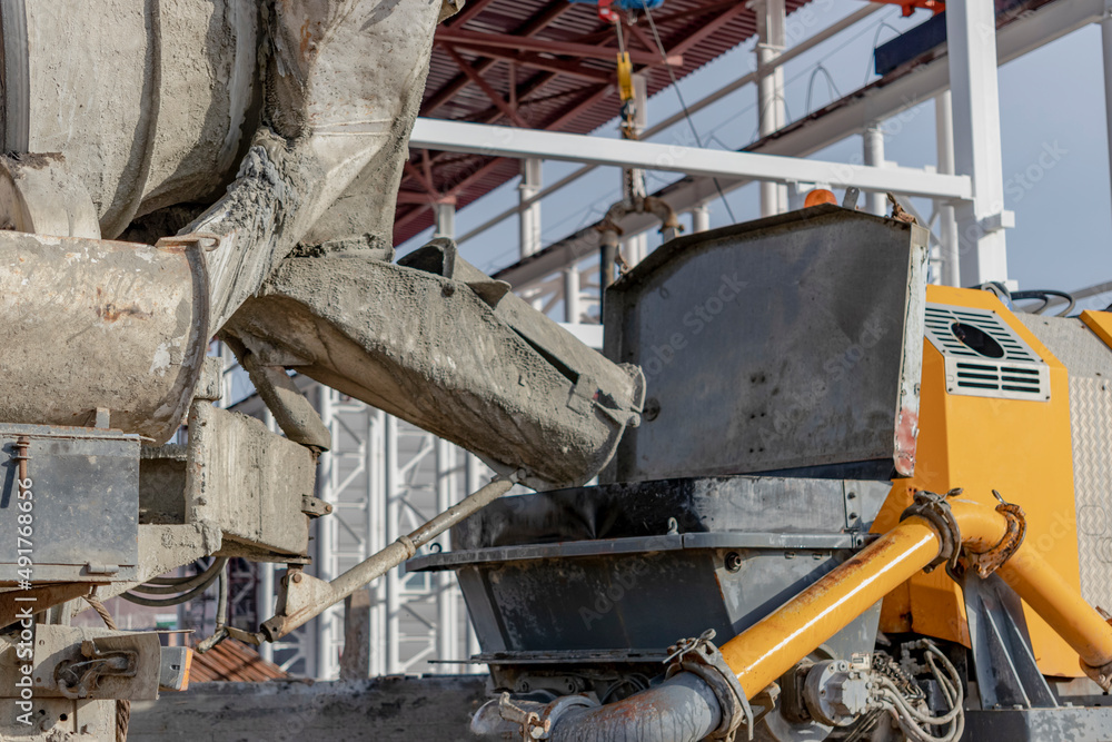 Fototapeta premium A concrete mixer truck pours mortar into a concrete pump at a construction site. Supply of concrete and mortar for the production of monolithic reinforced concrete works. Close-up.