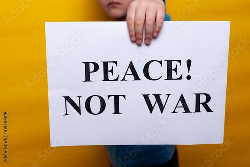 A child in a blue T shirt holds a poster with appeals for peace on a yellow background. no face, close-up