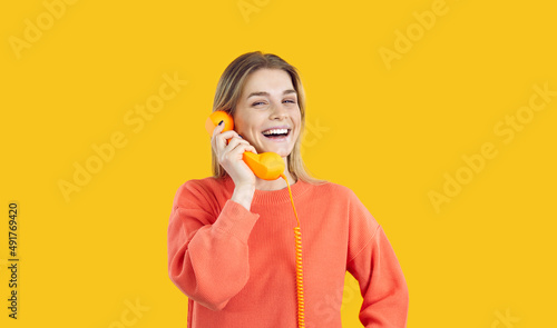 Foto Portrait of joyful young woman talking on landline phone isolated on yellow background
