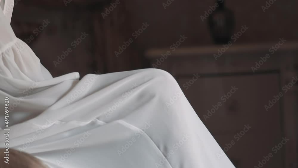 Young woman wraps up bare legs with elegant white dressing gown sitting on bed in hotel room close view. Attractive lady in stylish luxury lingerie Young woman wraps up bare legs with elegant white dressing gown sitting on bed in hotel room close view. Attractive lady in stylish luxury lingerie
