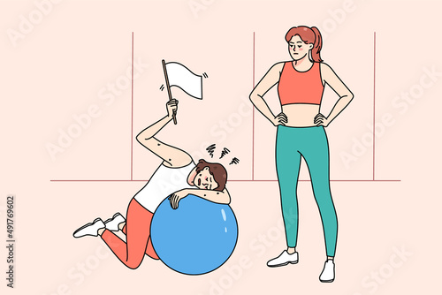 Tired woman rest lying on fitness ball after workout with personal trainer in sports club. Exhausted girl show white flag feel fatigue and weakness at sport training in gym. Sporty lifestyle. 