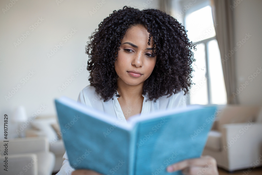 Young beautiful African American woman holding book, University student studying, learning language. leisure, literature and people concept - smiling african american woman reading book at home Young beautiful African American woman holding book, University student studying, learning language. leisure, literature and people concept - smiling african american woman reading book at home