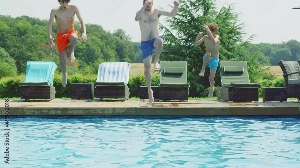 Father jumping into outdoor swimming pool on summer vacation together - shot in slow motion