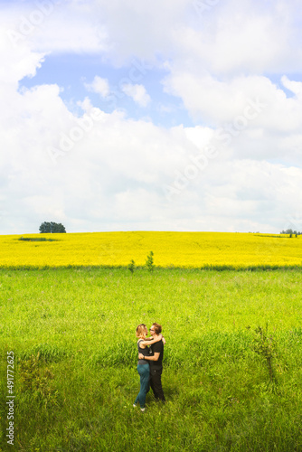 couple standing in the middle of a beautiful field full of yellow flowers. Yellow field of flowering rapeseed with cloudy blue sky - brassica napus - plant for green energy, medicine.