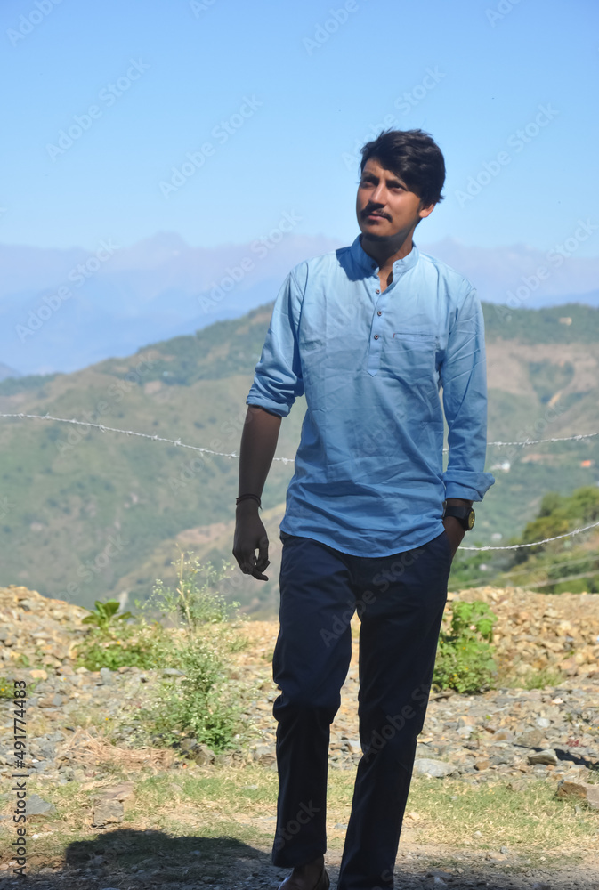 Full length front view of a young guy walking in hilly area with hand on pocket and looking away with copy space Full length front view of a young guy walking in hilly area with hand on pocket and looking away with copy space