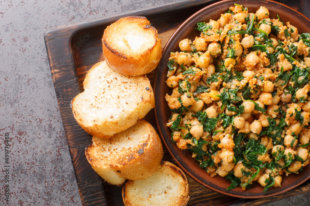 Spanish spinach and chickpeas served with toasts closeup in the plate on the table. Horizontal top view from above
