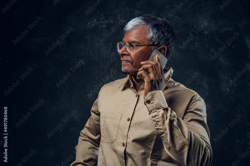 Serious grandpa talking on his cellphone against dark background Serious grandpa talking on his cellphone against dark background