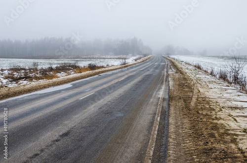 Winter road in Russia stretching into the distance into the fog. Mud and slush on the side of the road during the thaw.