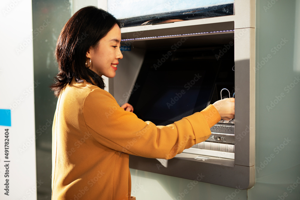 Happy smiling young woman withdrawing money from credit card. Young woman typing pin code on keypad of ATM machine. Happy smiling young woman withdrawing money from credit card. Young woman typing pin code on keypad of ATM machine.