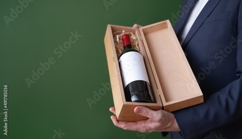 Male hands holding wooden gift box with bottle of red wine.Unrecognizable man offering,advertising alcohol drink on green background. Copy space