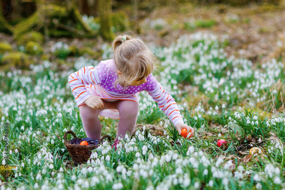 Little girl in pink dress making egg hunt in spring forest on sunny day, outdoors. Cute happy child with lots of snowdrop flowers and colored eggs. Springtime, christian holiday concept. Little girl in pink dress making egg hunt in spring forest on sunny day, outdoors. Cute happy child with lots of snowdrop flowers and colored eggs. Springtime, christian holiday concept.