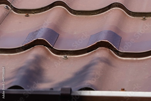 Repair of holes on metal roof with TechnoNIKOL self-adhesive waterproofing bituminous tape. Close-up. Patches from waterproofing tape on holes from self-tapping screws after torn off snow retainers. photo