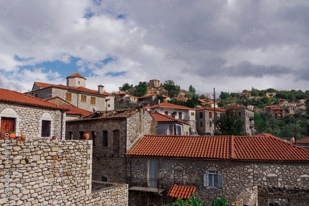 Greek village with traditional stone built houses against sky with clouds. Day view of historic settlement with red roof tiles residences in Karytaina, Arcadia Peloponnese.