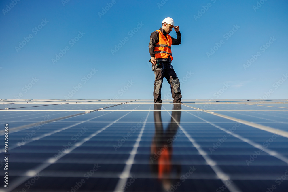 A worker walking around roof and checking on screws on solar panels. A worker walking around roof and checking on screws on solar panels.