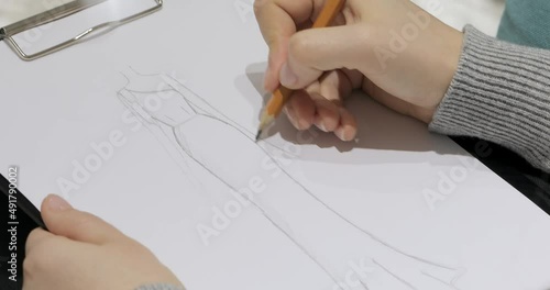 the hand of the designer draws with a graphite pencil on white paper a sketch of the design of an evening wedding dress. A close-up shot through a brilliant crystal prism. focus translation. macro