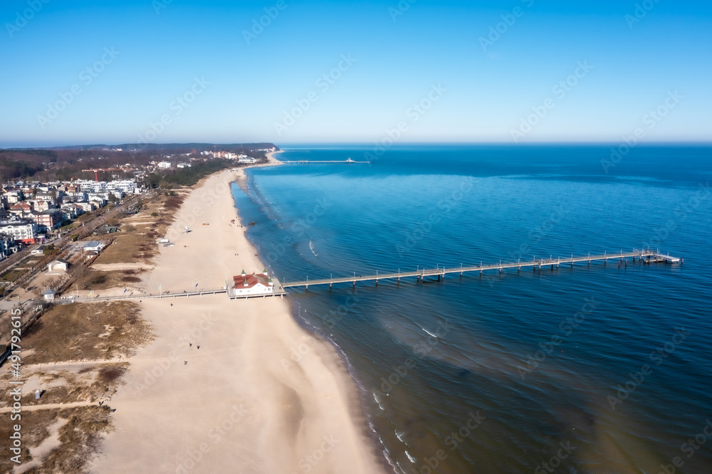 Aerial view of the coastline around city of Ahlbeck on the peninsula Usedom in Germany during a sunny day in early spring. Pier juts out into the Baltic Sea. The famous building are behind the beach.