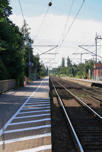 Perspective view of train tracks and platform at train station in summer with clouds in sunny blue sky background. No people.